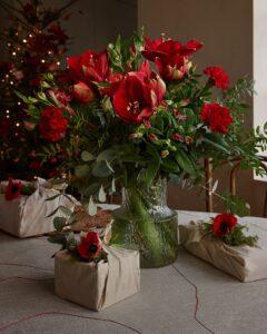 Decemberbuketten med röda julblommor. Amaryllis, nejlikor, alstroemeria och juligt grönt.