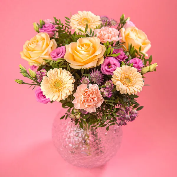 Aprilbuketten från Euroflorist, med gerbera, rosor och nejlikor i ljust gult, aprikost och rosa. Här, en bild på buketten i en rund glasvas.